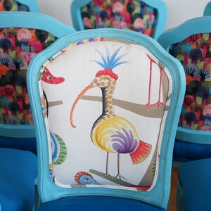May include: Set of turquoise blue chairs with colorful patterned fabric upholstery. One chair features a white fabric with a colorful bird design. The other chairs feature a colorful pattern of trees and flowers.