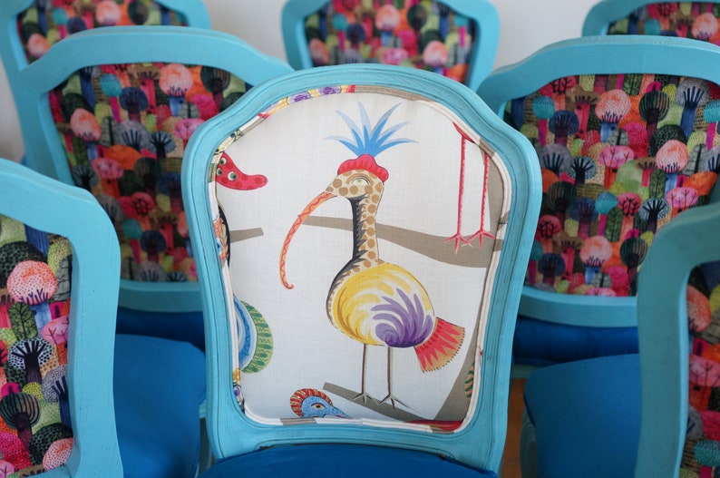 May include: Set of turquoise blue chairs with colorful patterned fabric upholstery. One chair features a white fabric with a colorful bird design. The other chairs feature a colorful pattern of trees and flowers.