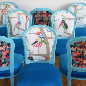 May include: Six turquoise blue dining chairs with different colorful patterned fabric backrests. The chairs have a classic design with a curved back and a padded seat.