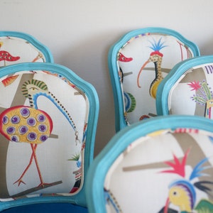 May include: A set of turquoise blue chairs with white fabric seats featuring a colorful bird pattern. The birds are stylized and have long necks and beaks.