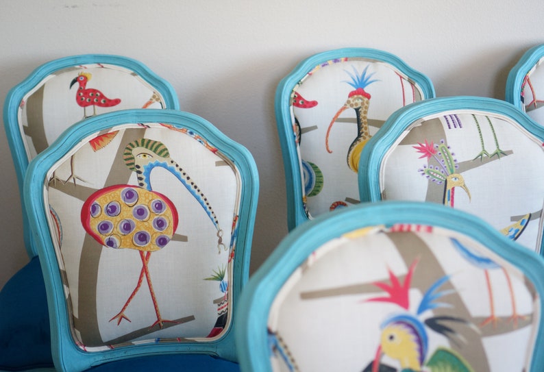 May include: A set of turquoise blue chairs with white fabric seats featuring a colorful bird pattern. The birds are stylized and have long necks and beaks.