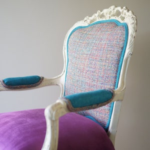 May include: A white, ornate chair with a turquoise and multi-colored patterned fabric seat and turquoise fabric armrests. The chair has a purple cushion on the seat.