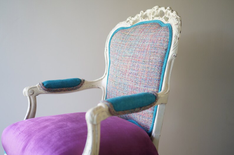 May include: A white, ornate chair with a turquoise and multi-colored patterned fabric seat and turquoise fabric armrests. The chair has a purple cushion on the seat.