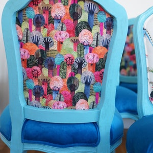 May include: A set of two turquoise blue dining chairs with a colorful forest print on the backrests and blue velvet seats.