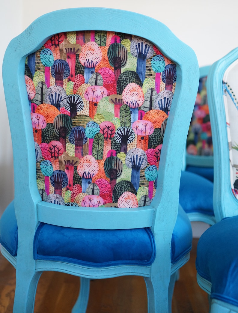 May include: A set of two turquoise blue dining chairs with a colorful forest print on the backrests and blue velvet seats.