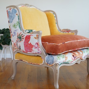 May include: A vintage armchair with a white and yellow fabric upholstery featuring a colorful tiger print. The chair has a light gray painted frame and a brown cushion.