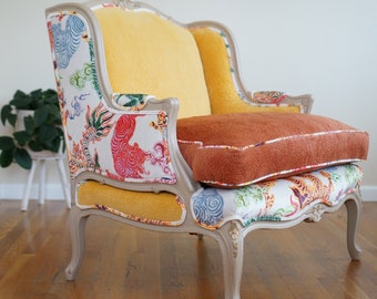 May include: A vintage armchair with a white and yellow fabric upholstery featuring a colorful tiger print. The chair has a light gray painted frame and a brown cushion.
