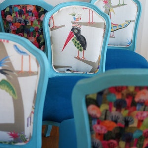May include: Four turquoise blue chairs with different patterned fabric upholstery. The chairs have a curved back and a white fabric insert with a colorful bird design.