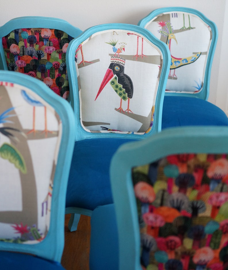 May include: Four turquoise blue chairs with different patterned fabric upholstery. The chairs have a curved back and a white fabric insert with a colorful bird design.