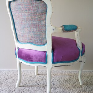 May include: A white, ornate chair with a teal and purple velvet seat and a patterned back. The chair is sitting on a light gray carpet.