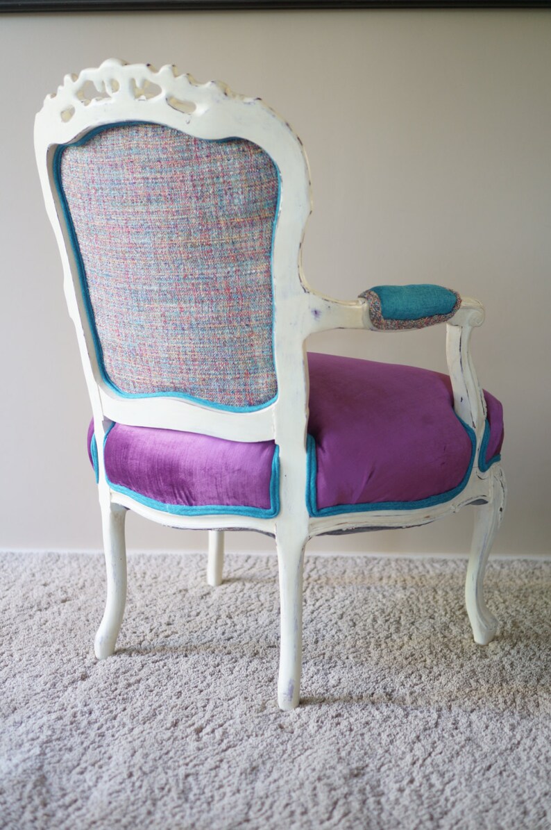 May include: A white, ornate chair with a teal and purple velvet seat and a patterned back. The chair is sitting on a light gray carpet.