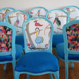 May include: Six turquoise blue dining chairs with ornate carved legs and backs. The chairs have different patterned fabric upholstery featuring colorful birds and trees.