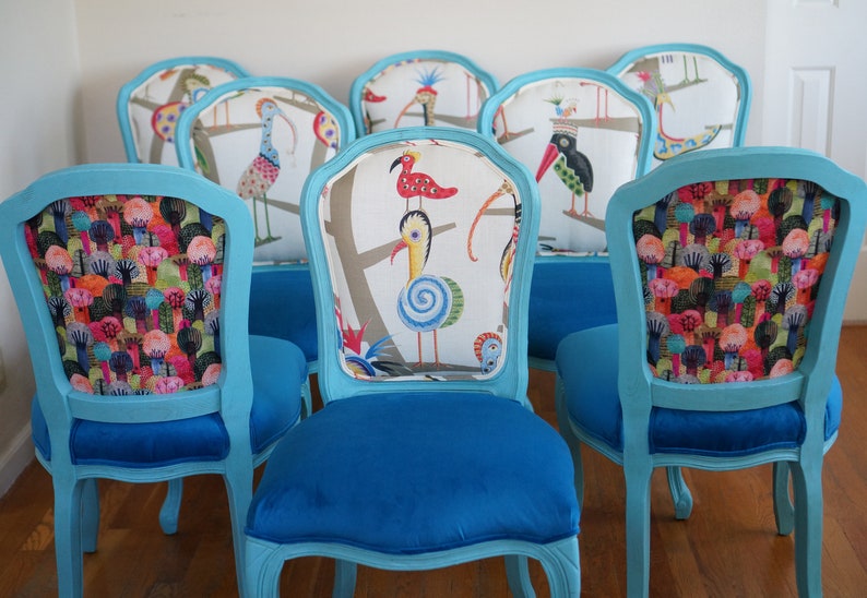 May include: Six turquoise blue dining chairs with ornate carved legs and backs. The chairs have different patterned fabric upholstery featuring colorful birds and trees.