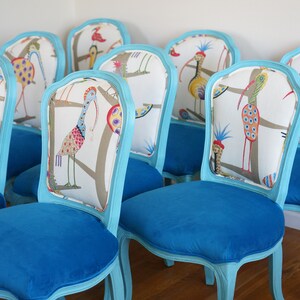 May include: A set of eight turquoise blue chairs with white and colorful bird patterned upholstery. The chairs have a classic French design with a curved back and ornate legs.