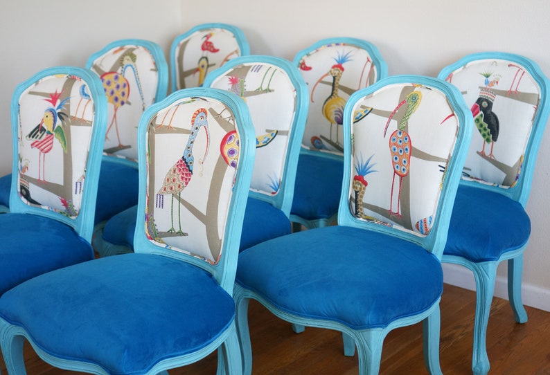 May include: A set of eight turquoise blue chairs with white and colorful bird patterned upholstery. The chairs have a classic French design with a curved back and ornate legs.