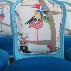 May include: A blue upholstered chair with a white fabric back featuring a colorful bird design. The chair has a curved back and a blue painted frame.