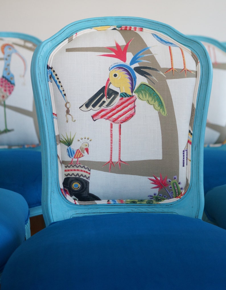 May include: A blue upholstered chair with a white fabric back featuring a colorful bird design. The chair has a curved back and a blue painted frame.