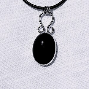 May include: A silver pendant necklace featuring a polished, oval black gemstone. The pendant is suspended from a black cord. The silver setting has a decorative, open design above the gemstone.