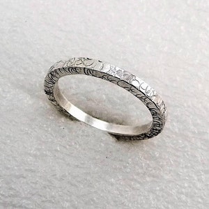 May include: A silver band ring with a textured surface. The ring is simple and elegant.