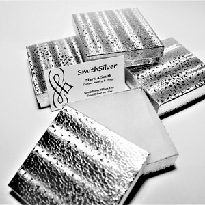 May include: Five silver gift boxes with a textured surface. The boxes are stacked on top of each other. A business card with the text "SmithSilver Mark A Smith Custom Jewelry & Design SmithSilver2011 on Etsy SmithSilver on eBay" is visible on top of the boxes.