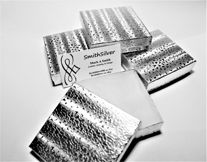 May include: Five silver gift boxes with a textured surface. The boxes are stacked on top of each other. A business card with the text "SmithSilver Mark A Smith Custom Jewelry & Design SmithSilver2011 on Etsy SmithSilver on eBay" is visible on top of the boxes.