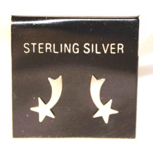 May include: A pair of sterling silver earrings featuring a shooting star design. The earrings are displayed on a black card with the words "Sterling Silver" printed on it.