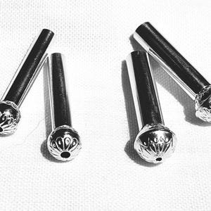 May include: Four silver-toned metal pins with cylindrical shafts and rounded, decorative heads featuring a radial, petal-like pattern. Each head has a small, centered hole, and the metal surfaces exhibit a polished, reflective finish.