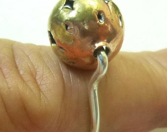 May include: A silver ring with a gold sphere attached. The sphere has a textured surface with small holes.
