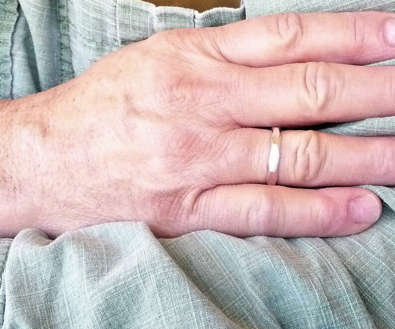 May include: A close-up of a person's hand wearing a silver band ring. The ring is simple and has a slightly textured surface.