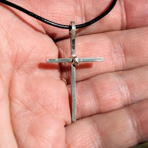 May include: A silver cross pendant with a knotted design, hanging from a black leather cord.