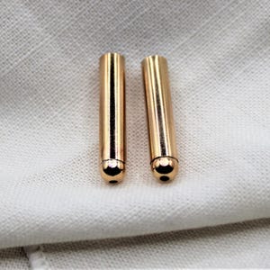 May include: Two gold-colored metal cord ends with rounded tips.
