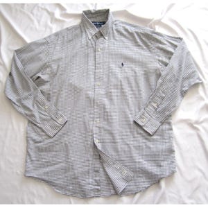 May include: A long-sleeved button-down shirt in a gray and white checkered pattern. The shirt has a button-down collar and a small embroidered logo on the chest. The shirt is made of a lightweight fabric.