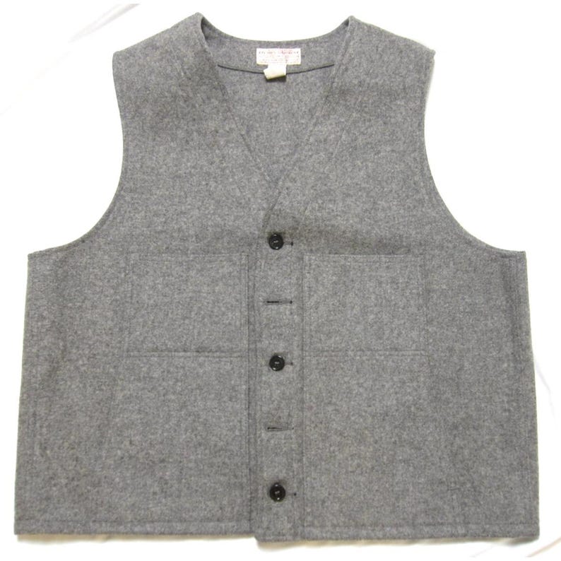 Puede incluir: Un chaleco de lana gris con cuello en V y cuatro botones negros en la parte delantera. El chaleco tiene dos bolsillos delanteros y una peque&ntilde;a etiqueta cerca del cuello. Prenda de color neutro, adecuada para combinar.