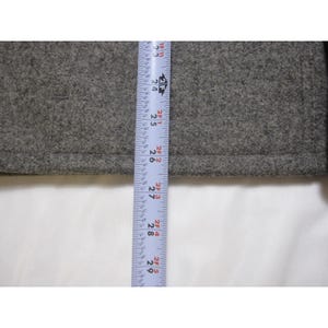 Puede incluir: Primer plano de una tela gris con una cinta m&eacute;trica. La cinta muestra medidas de 58 cm a 74 cm. La tela parece ser lana texturizada o un material similar.