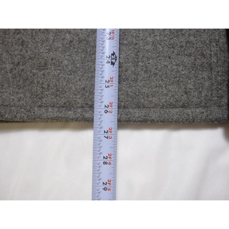 Puede incluir: Primer plano de una tela gris con una cinta m&eacute;trica. La cinta muestra medidas de 58 cm a 74 cm. La tela parece ser lana texturizada o un material similar.