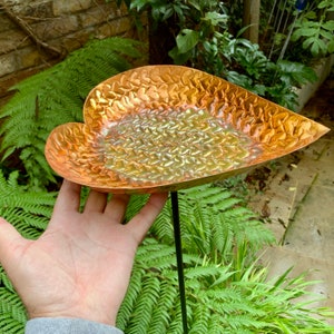 May include: A heart-shaped copper bird bath with a hammered texture. The bath is mounted on a black metal stake.