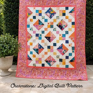 May include: A rectangular quilt featuring a central panel of white fabric with a repeating pattern of colourful floral squares and diamonds in shades of pink, orange, blue, and yellow, surrounded by a wide border with a pink and orange paisley print.