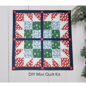 May include: A DIY mini quilt kit featuring a red, white, and green Christmas-themed quilt with a star pattern. The quilt is framed with a dark blue border and red trim. The text "DIY Mini Quilt Kit" is printed below the quilt.