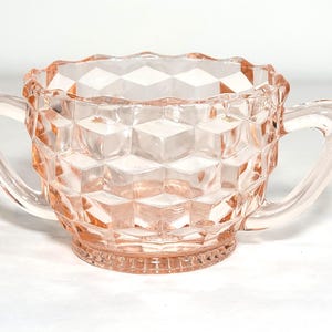 May include: A pink glass sugar bowl with a diamond pattern and two handles.