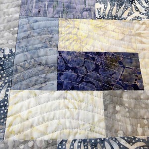 May include: A quilt made of various shades of blue and white fabric with a wavy quilting pattern.