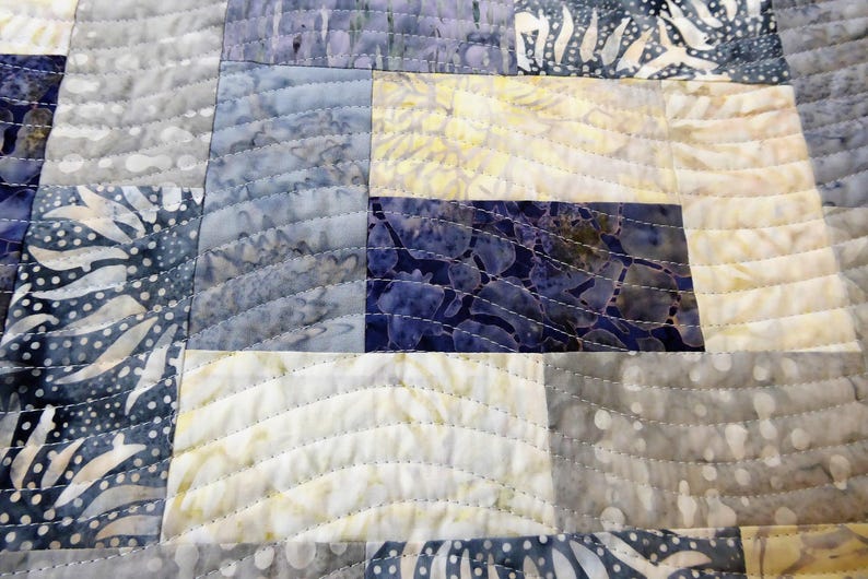 May include: A quilt made of various shades of blue and white fabric with a wavy quilting pattern.
