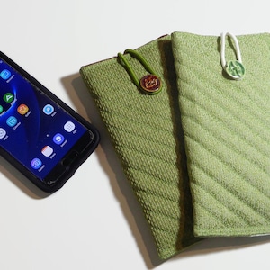 May include: Two green quilted phone cases with decorative buttons. One case has a brown button with a gold design, the other has a white button with a green design.