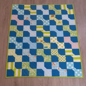 May include: A handmade quilt with a patchwork design. The quilt features a repeating pattern of blue, green, and white squares. Some squares have polka dots, stripes, or animal prints. The quilt is bordered with a green binding.