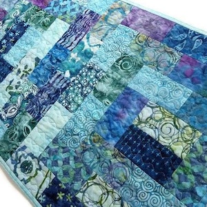 May include: A blue and green patchwork table runner with a chevron pattern. The runner is made of various fabrics with different patterns, including swirls, flowers, and geometric designs.