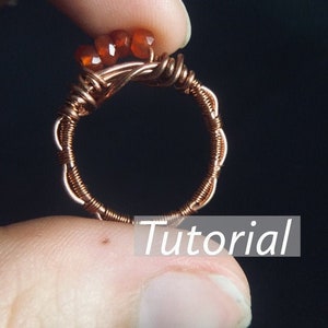 May include: A copper wire ring with a cluster of orange carnelian stones. The ring is on a finger and the word "Tutorial" is visible below the ring.