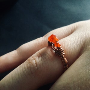 May include: A copper wire ring with three orange carnelian stones. The ring is on a person's finger.