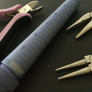 K&ouml;nnte beinhalten: Nahaufnahme eines violetten Ringmandrels mit Gr&ouml;&szlig;enmarkierungen von 5 bis 10. Auf dem Bild sind auch zwei Paar Schmuckzangen zu sehen. Ein Paar ist pink und das andere silber.