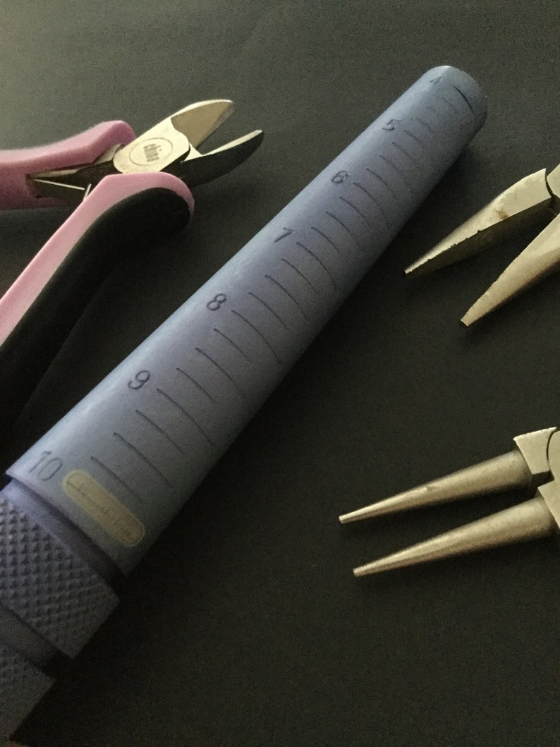 K&ouml;nnte beinhalten: Nahaufnahme eines violetten Ringmandrels mit Gr&ouml;&szlig;enmarkierungen von 5 bis 10. Auf dem Bild sind auch zwei Paar Schmuckzangen zu sehen. Ein Paar ist pink und das andere silber.