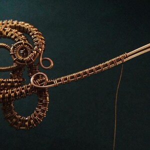 K&ouml;nnte beinhalten: Nahaufnahme einer Skulptur aus Kupferdraht mit komplizierten gewebten Mustern. Die Skulptur besteht aus d&uuml;nnem Kupferdraht und hat eine zarte, organische Form.