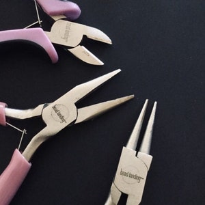 K&ouml;nnte beinhalten: Drei Paar Schmuckzangen mit rosa Griffen. Die Zangen sind mit "bead landing" beschriftet.